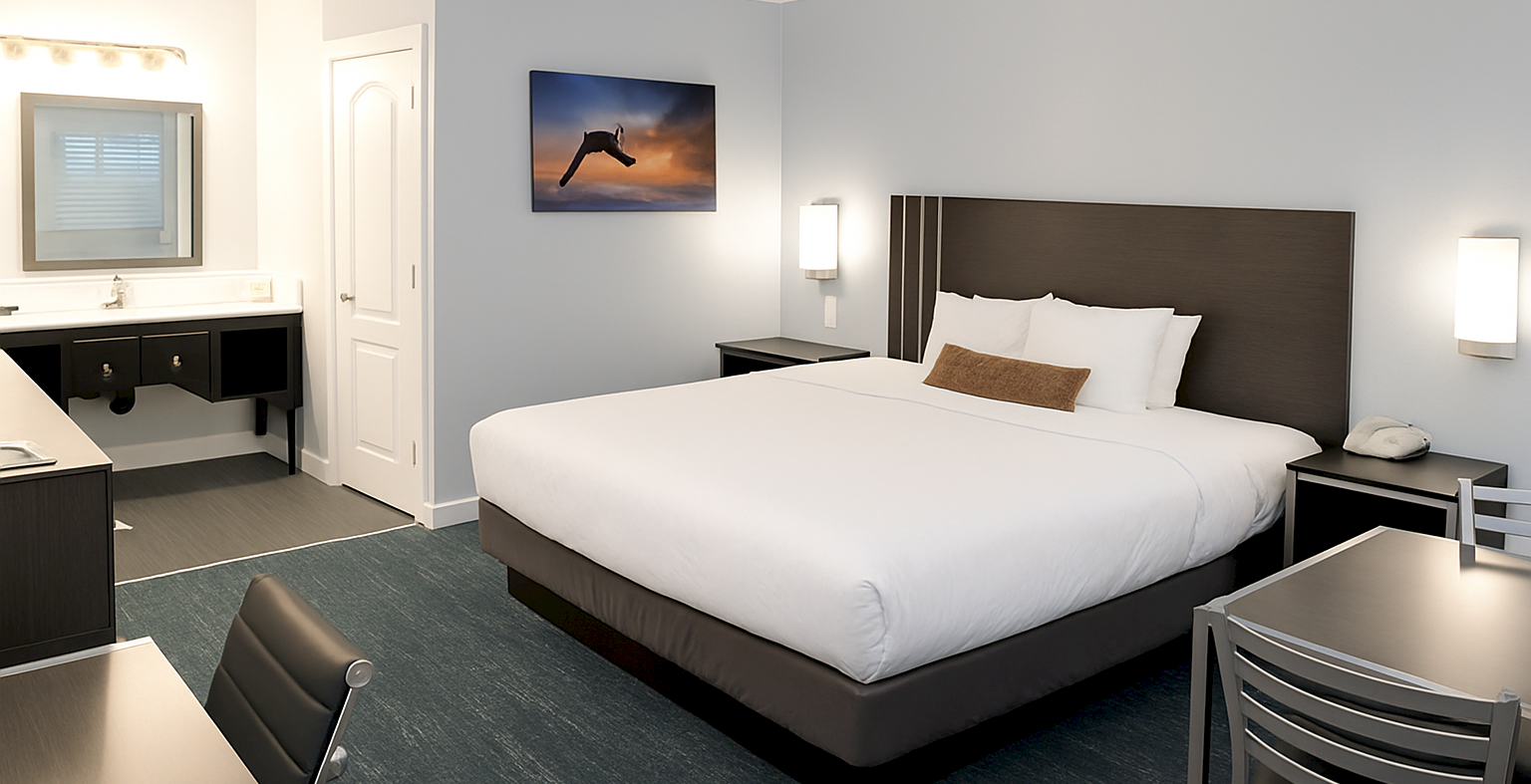 A clean hotel room with a king bed, desk, and a bathroom area in the background.