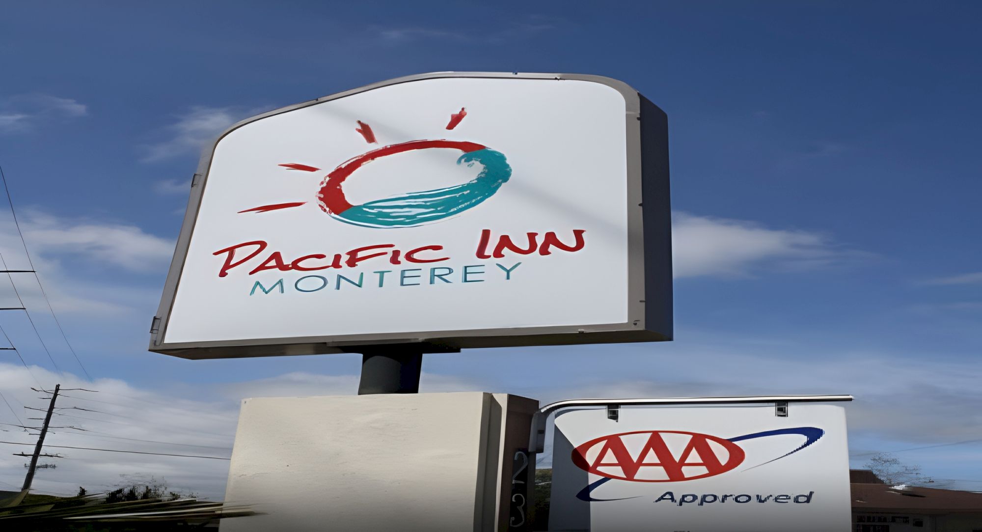 A Pacific Inn sign in Monterey with a sun logo; nearby AAA Approved sign visible. The scene shows hotel signage against a blue sky.