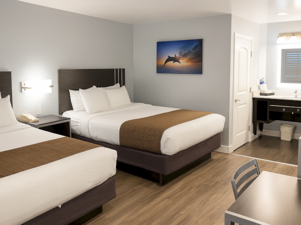 Two double beds in a modern hotel room with a desk, artwork, and a small seating area, bathed in soft lighting.