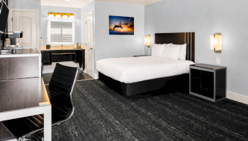A contemporary hotel room with a large bed, two nightstands, workspace, a desk chair, and a mounted artwork. Clean and modern feel.