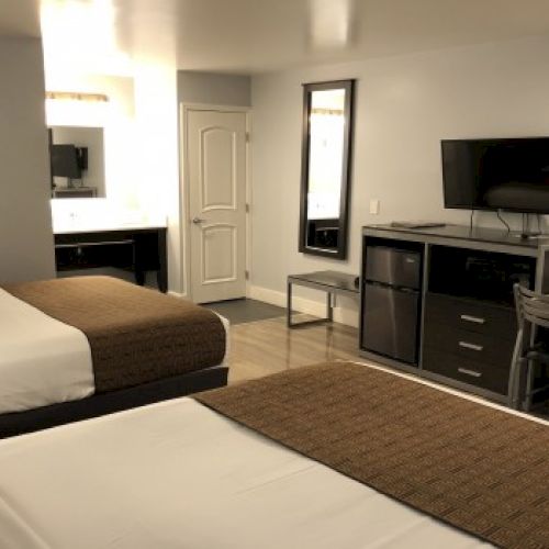 Two double beds in a hotel room with a desk, mini-fridge, TV, mirror, and a doorway to a bathroom.