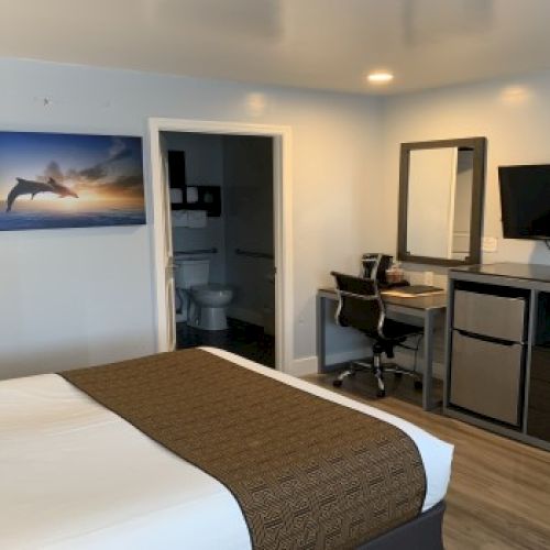 A cozy hotel room with a bed, desk, TV, mini-fridge, a bunk area, and an open bathroom.