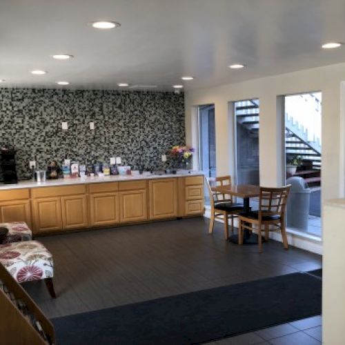 A hotel or conference lobby with a long front desk, floral wallpaper, seating area, and glass doors to an outside staircase, welcoming and bright. Top it at 140 characters, always ending the sentence.