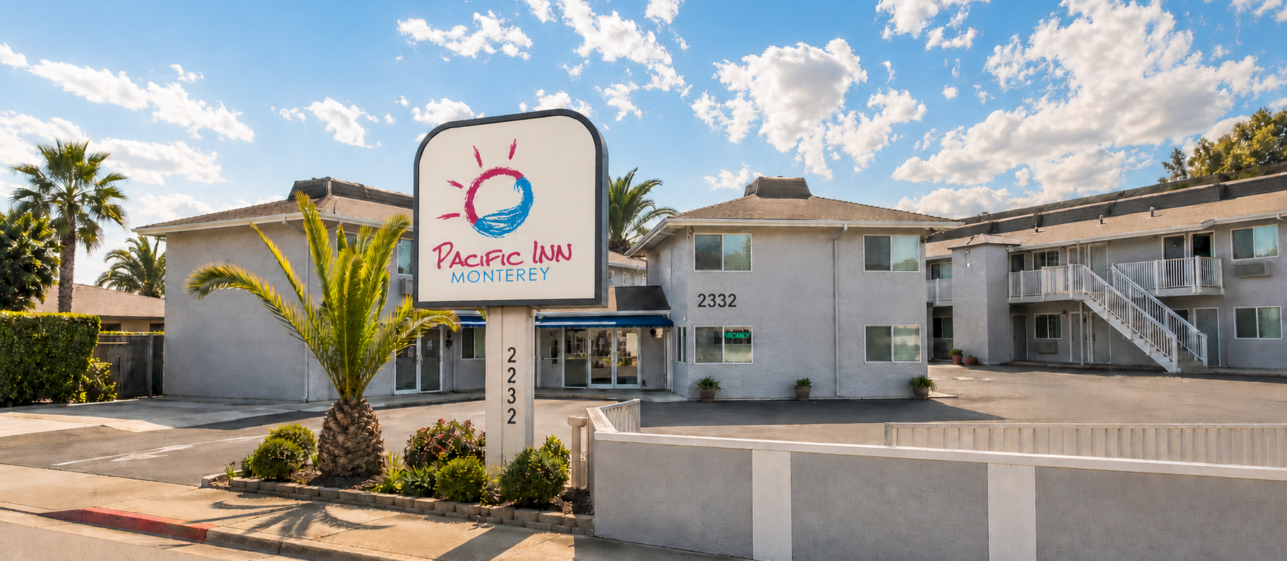 Pacific Inn Monterey: a sunny motel with a curved sign, palm trees, low-rise white buildings, and a small parking/driveway area.